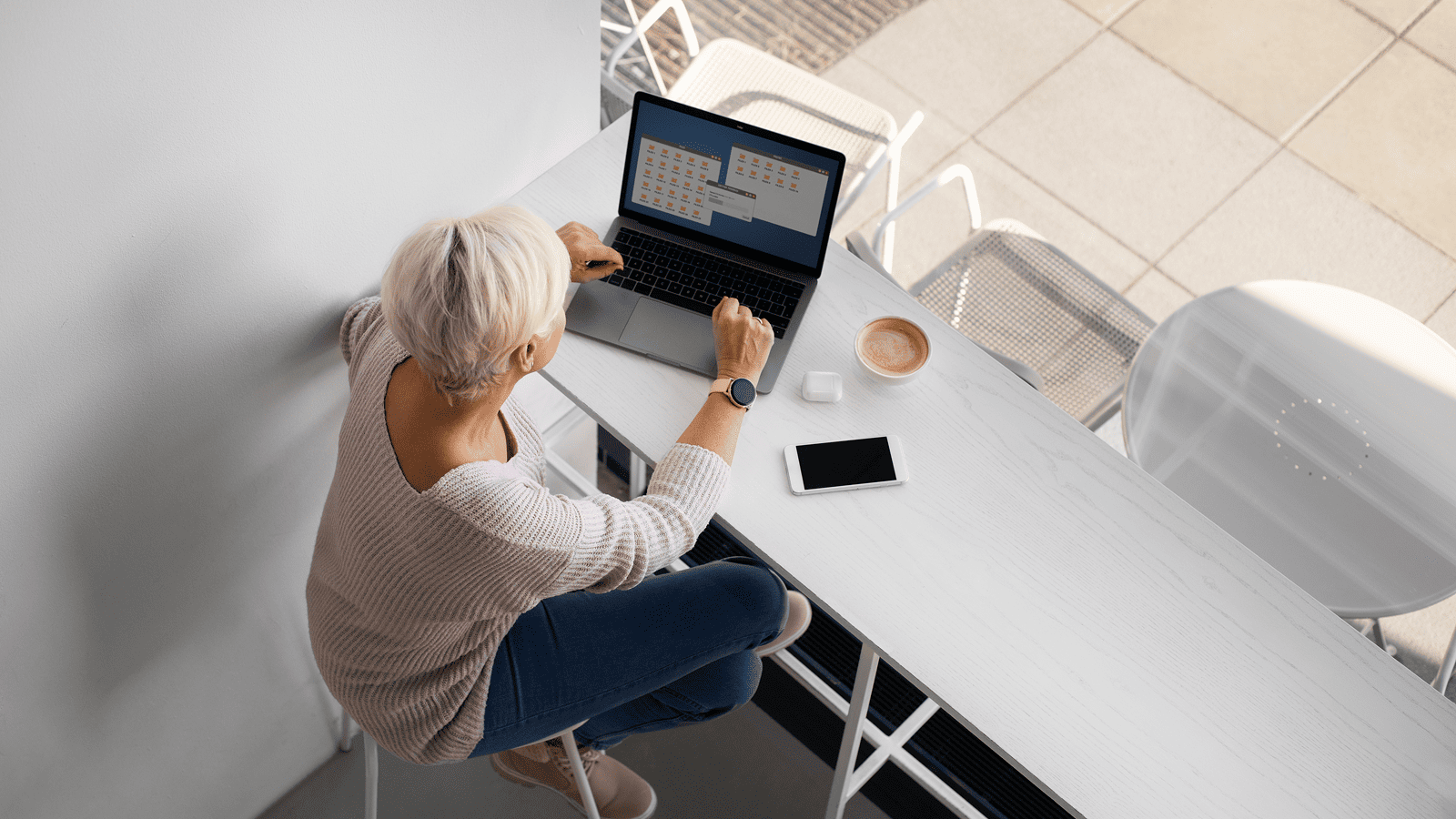 Женщина работает на ноутбуке за столом в кафе с кофе и смартфоном