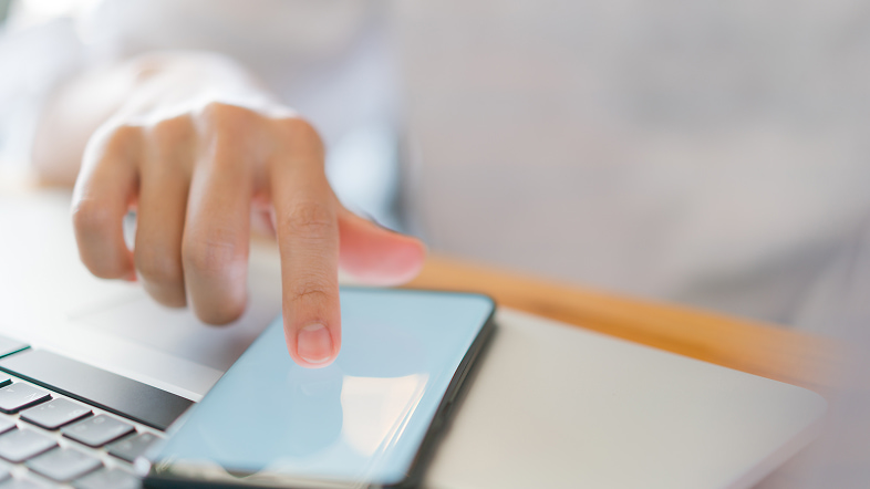 Рука касается светящегося стекла смартфона у кнопок ноутбука