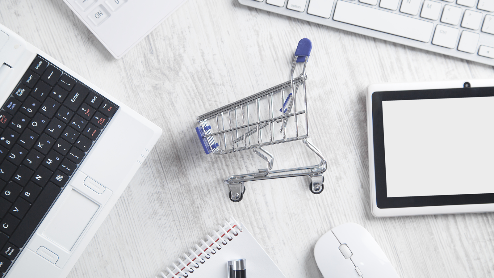 Вид сверху на рабочий стол с ноутбуком, планшетом, мышкой и моделью корзины для покупок