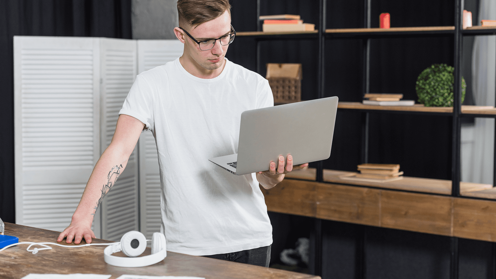 Молодой специалист в очках с ноутбуком у рабочего стола