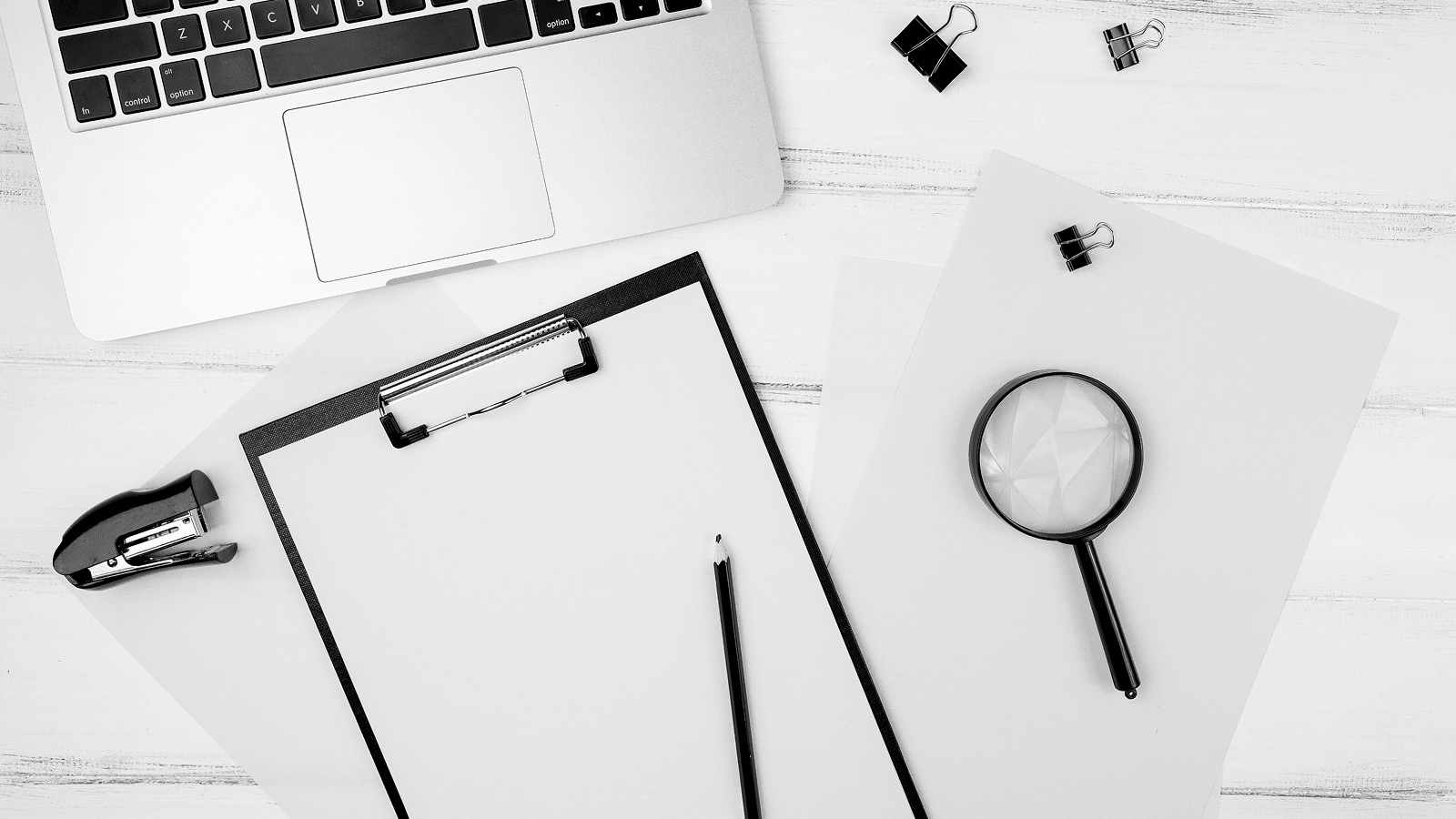 Рабочее место: ноутбук, клипборд с бумагой, карандаш и лупа