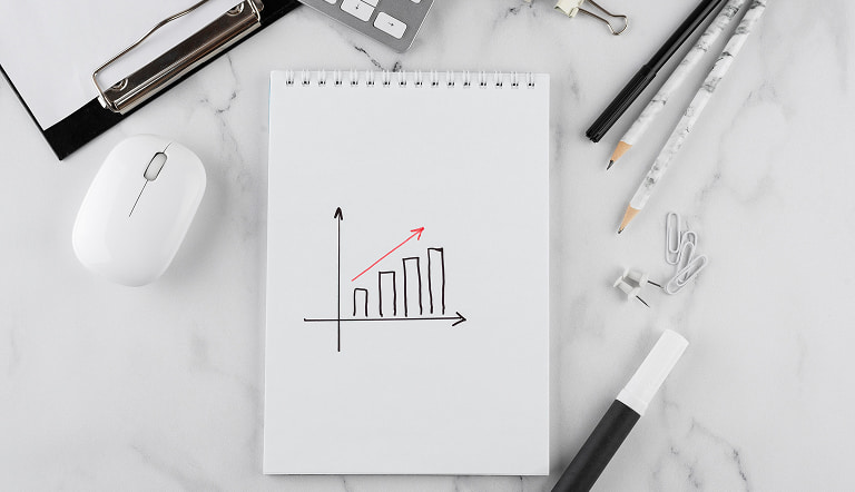 Блокнот с графиком роста на рабочем столе рядом с ноутбуком