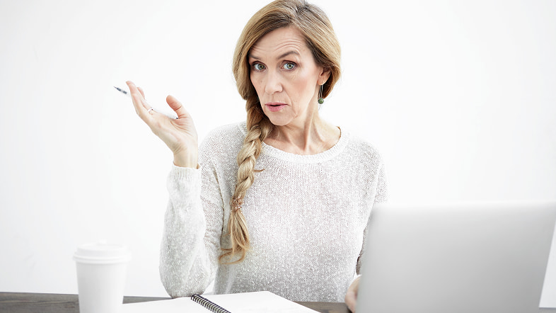 Женщина за ноутбуком с блокнотом делает жест рукой