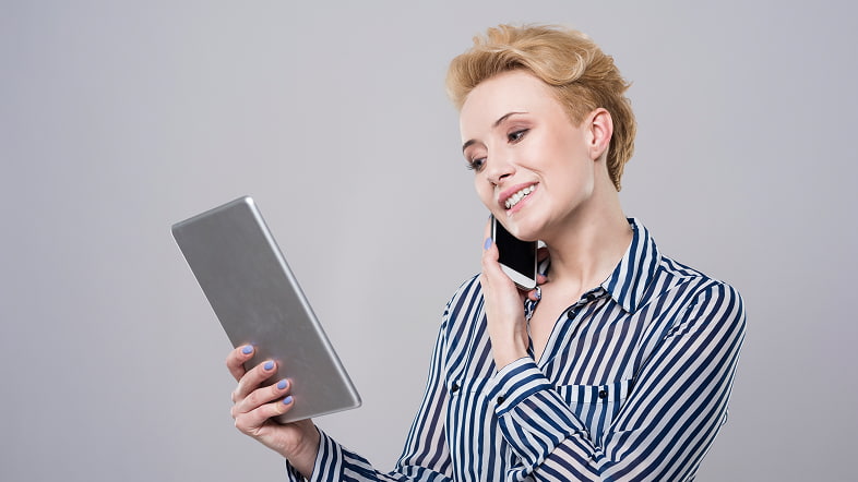 Женщина разговаривает по телефону и смотрит в планшет