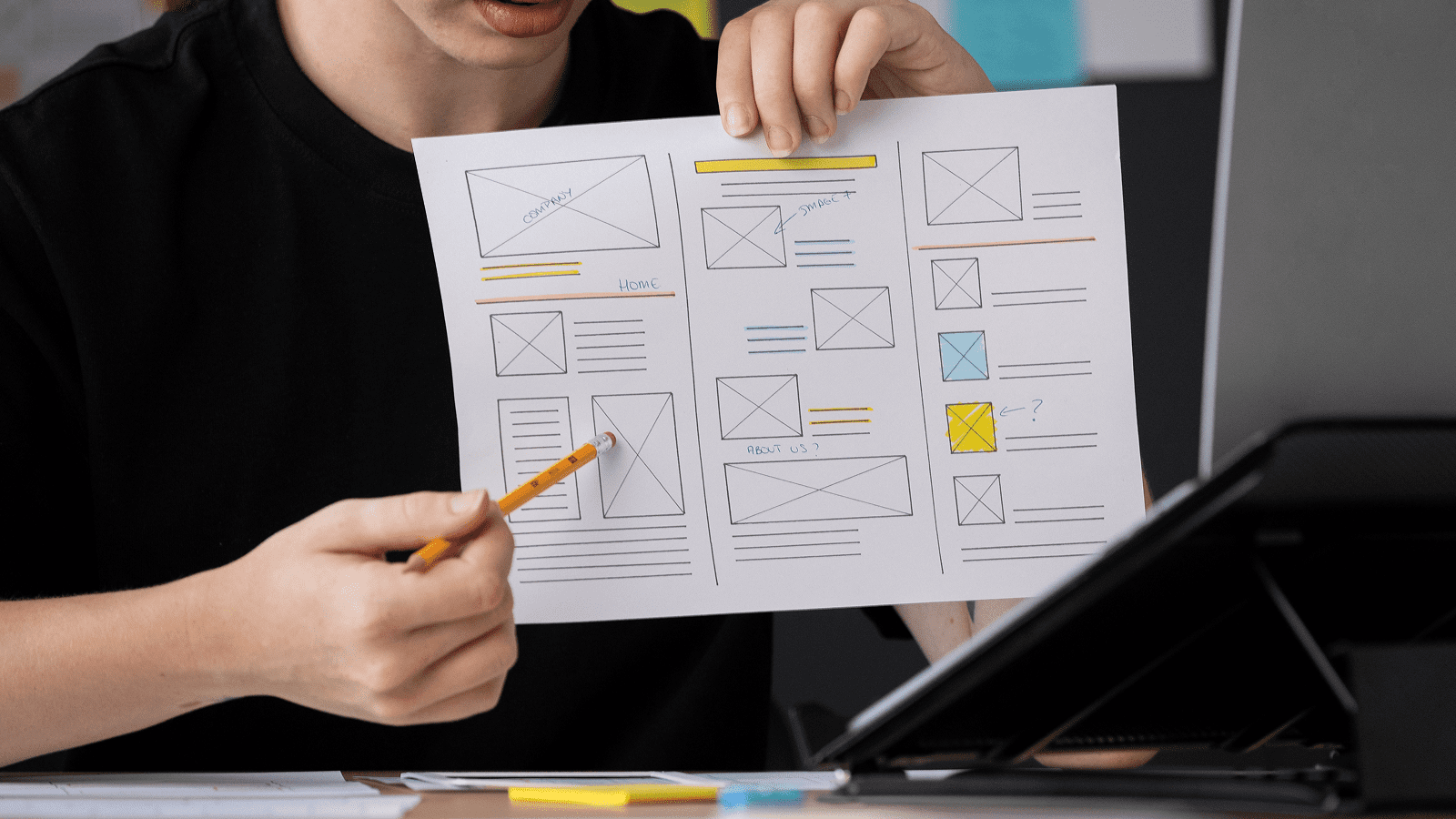 Женщина карандашом показывает прототип страницы корпоративного сайта на бумаге.
