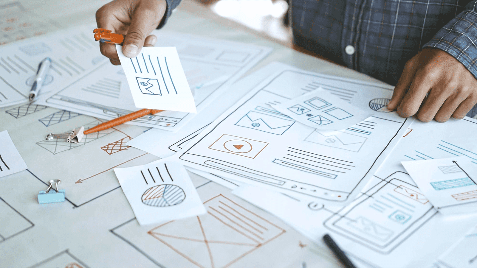 Человек расставляет бумажные прототипы интерфейса одностраничного сайта на столе