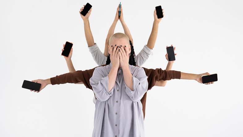 Человек закрывает лицо, вокруг подняты руки со смартфонами
