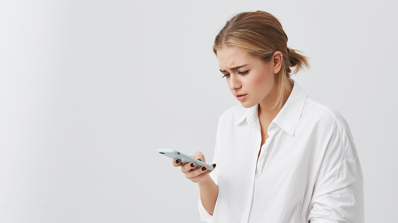 Женщина смотрит на смартфон с недоумением