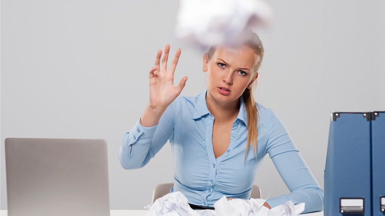 Женщина за столом с ноутбуком среди скомканной бумаги и папок