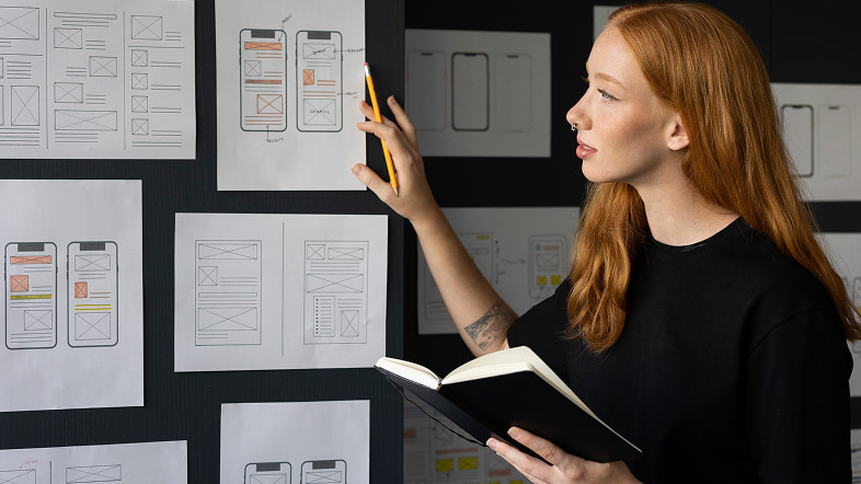 Женщина рассматривает листы с набросками вида страниц на стене