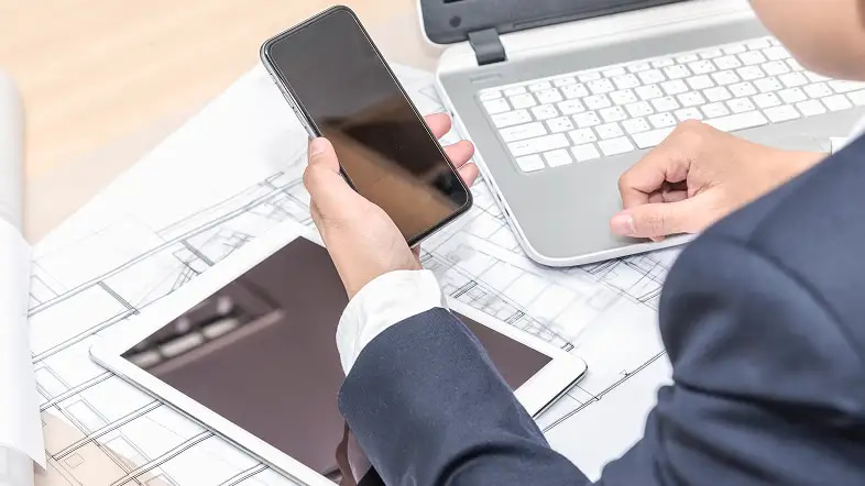 Человек держит смартфон рядом с ноутбуком и планшетом