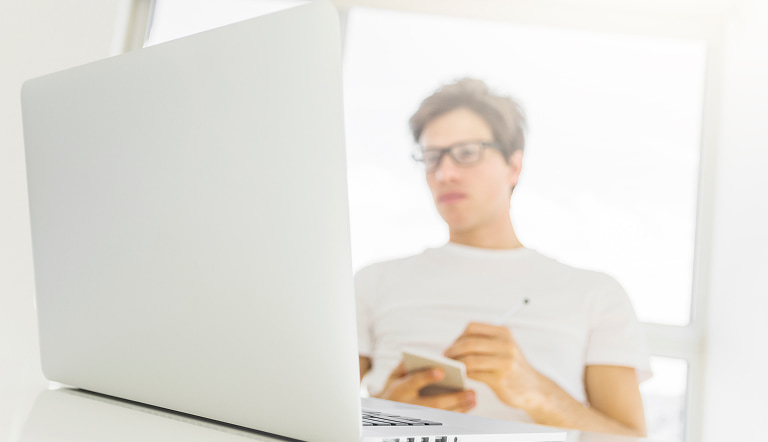 Мужчина с ноутбуком держит блокнот дома за столом