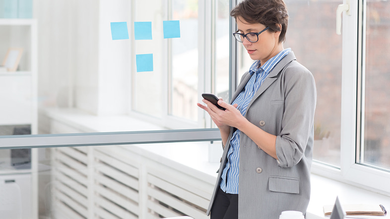 Женщина в офисе смотрит мобильный телефон рядом с листками заметок