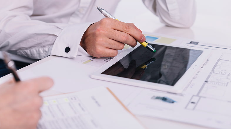 Рука с указкой над планшетом среди бумаг и чертежей