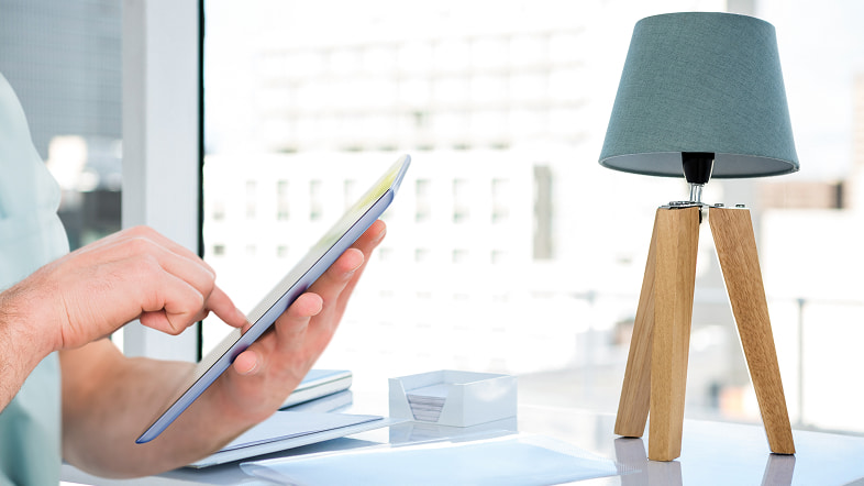 Человек держит планшет за столом у светильника