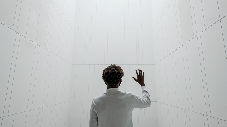 Человек в светлом помещении смотрит на высокие стены и поднимает руку