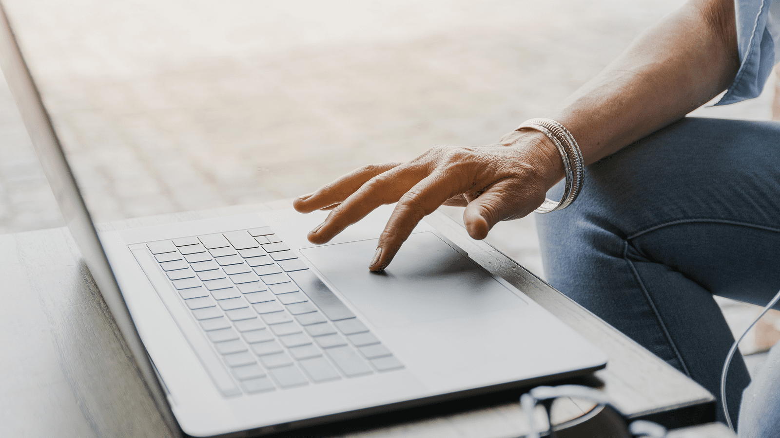 Рука человека касается трекпада ноутбука на столе рядом с очками.