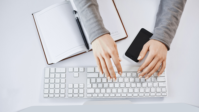 Работа за компьютером: руки на клавиатуре, смартфон и блокнот