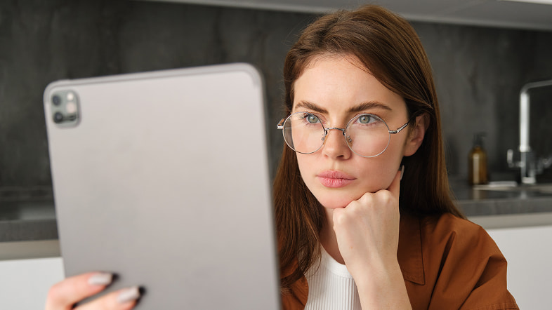 Женщина в очках смотрит на планшет, опираясь на руку